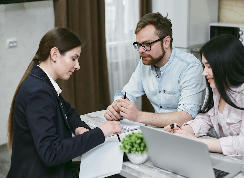 A high-net-worth couple consults with a family office professional in a modern office setting, discussing tailored financial strategies for wealth management, estate planning, and tax efficiency. This reflects the importance of personalized financial services in ensuring effective strategy execution for high-net-worth individuals.