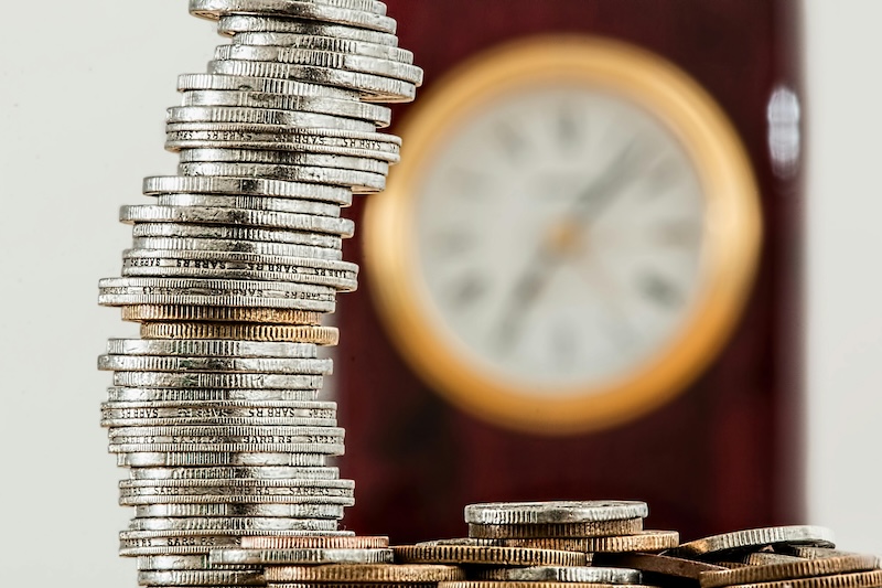 A stack of silver coins leaning against a blurred background featuring a clock, symbolizing the relationship between time and financial management. This image represents the hidden costs of wealth mismanagement and the importance of family offices in preserving and executing financial strategies efficiently.
